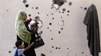 Una mujer palestina y sus hijos pasan frente a un muro agujereado por armas de fuego
