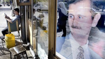 Reflejo de una mujer siria en el retrato del presidente sirio Bashar al-Assad en el escaparate de una tienda
