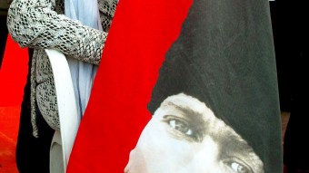 anciana sujetando una bandera de su país, con una imagen de Atatürk